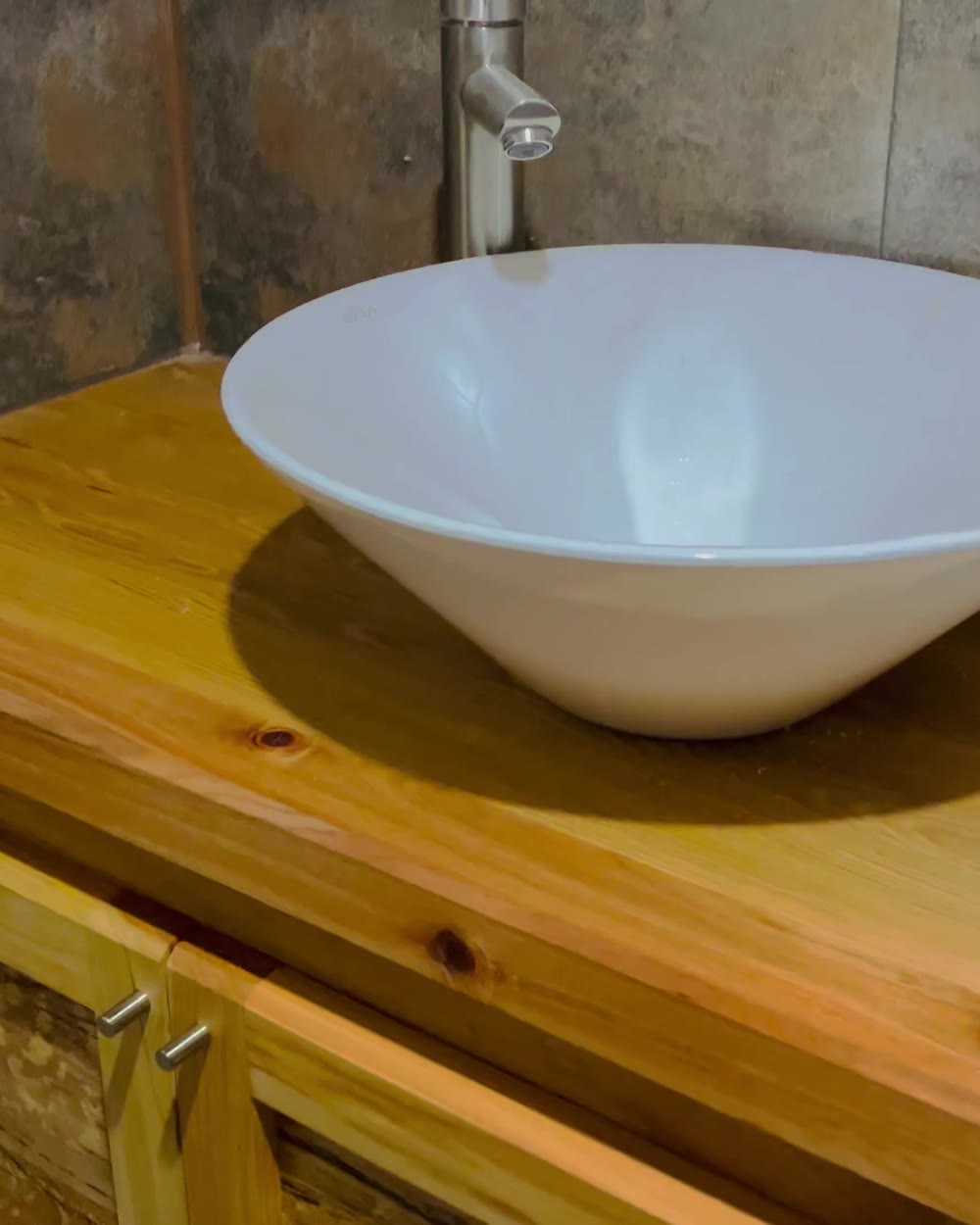 Detalle de un mueble de baño de madera con lavamanos de loza y grifería